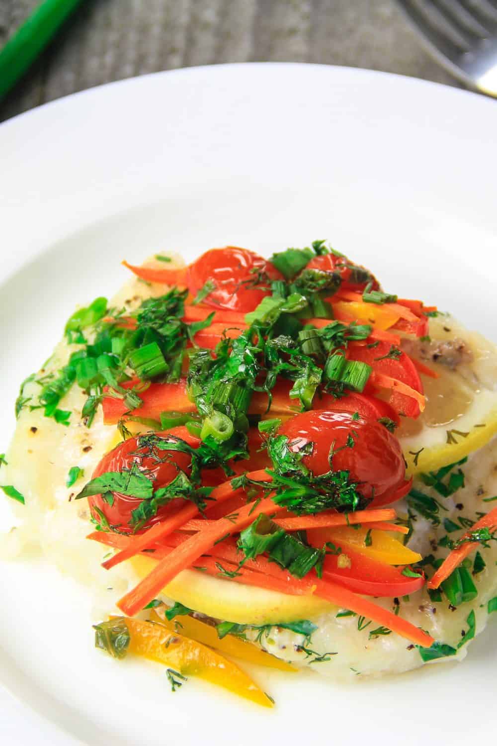 baked cod on a plate with lemon and roasted peppers and tomatoes