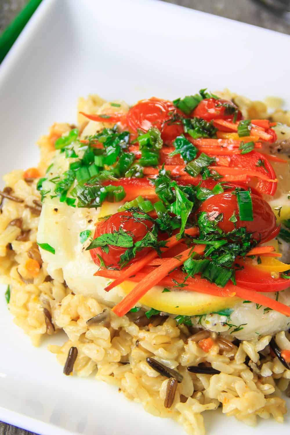 baked cod on a plate with lemon and roasted peppers and tomatoes