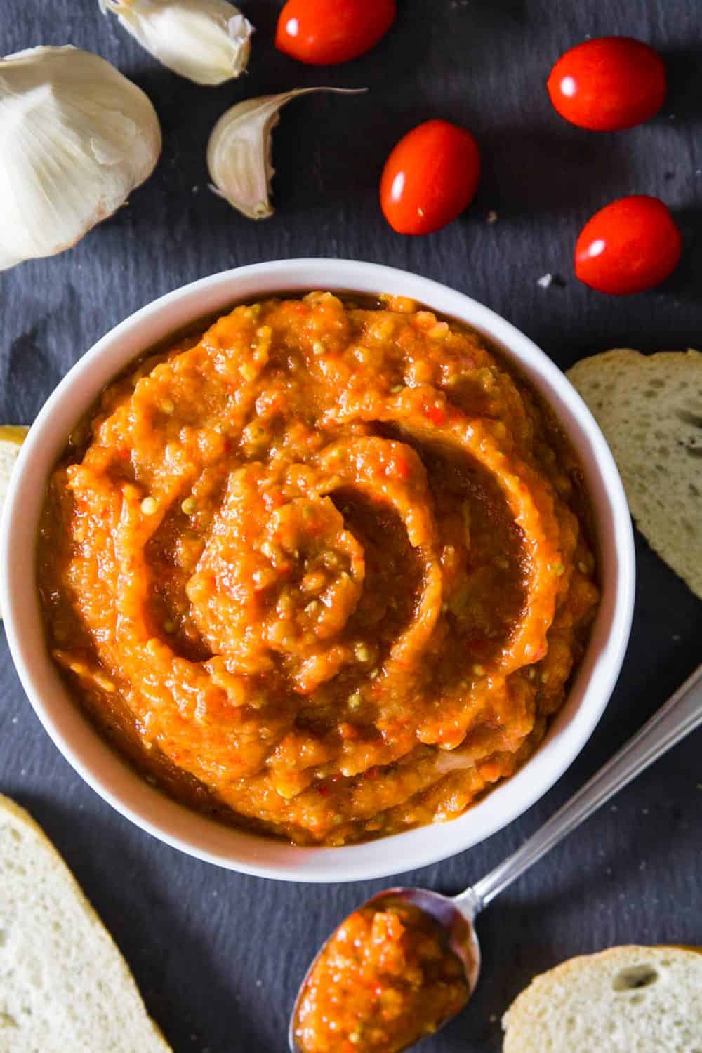 eggplant spread ikra, in a white bowl with tomatoes and bread around