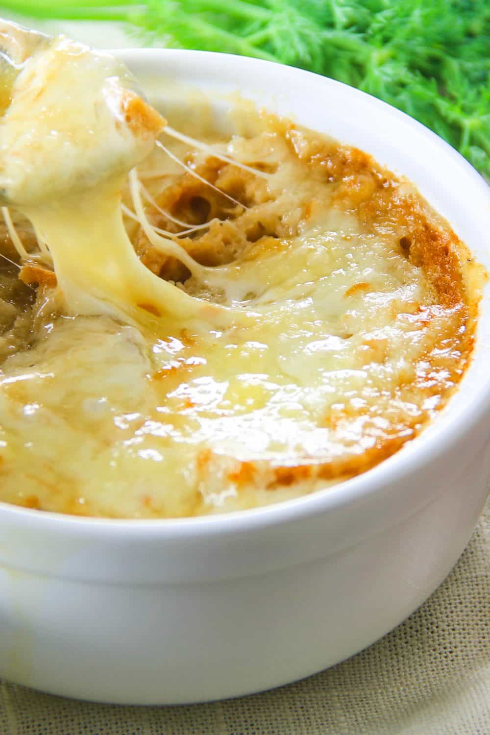 A close up of a cheese pull showing the broiled cheese on top of the french onion soup.