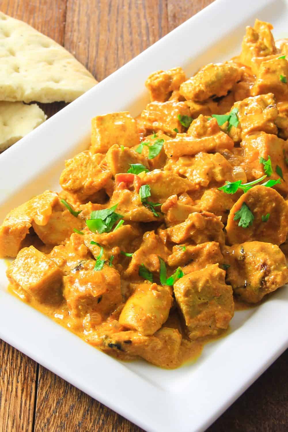 This Indian Butter Chicken Recipe makes a delicious dish full of rich spices and flavors. The yogurt marinade and sauce will give your chicken an amazing flavor that you're going to love. #indianbutterchicken #butterchicken #indianfood #bestbutterchicken Close up of white plate filled with Indian Butter chicken with some parsley on top and bread to the side.