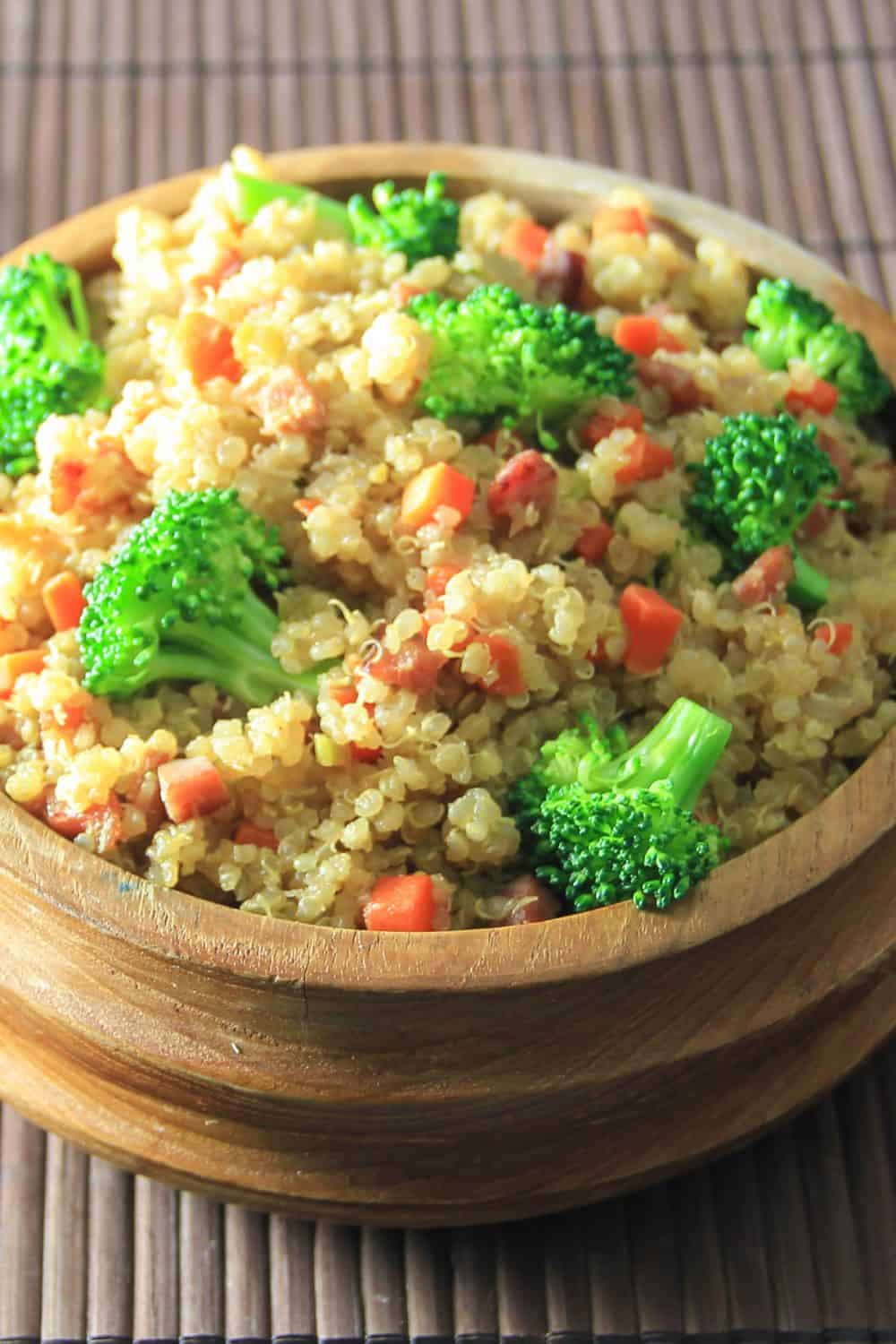 Fluffy quinoa fried recipe is a delicious way to enjoy fried rice minus the gluten. It's so tasty you wont even think of it as a substitute. #quinoafriedrice #friedrice #healthyfriedrice #quinoarecipe #friedquinoa close up image of quinoa fried rice in a wooden bowl on a bamboo mat