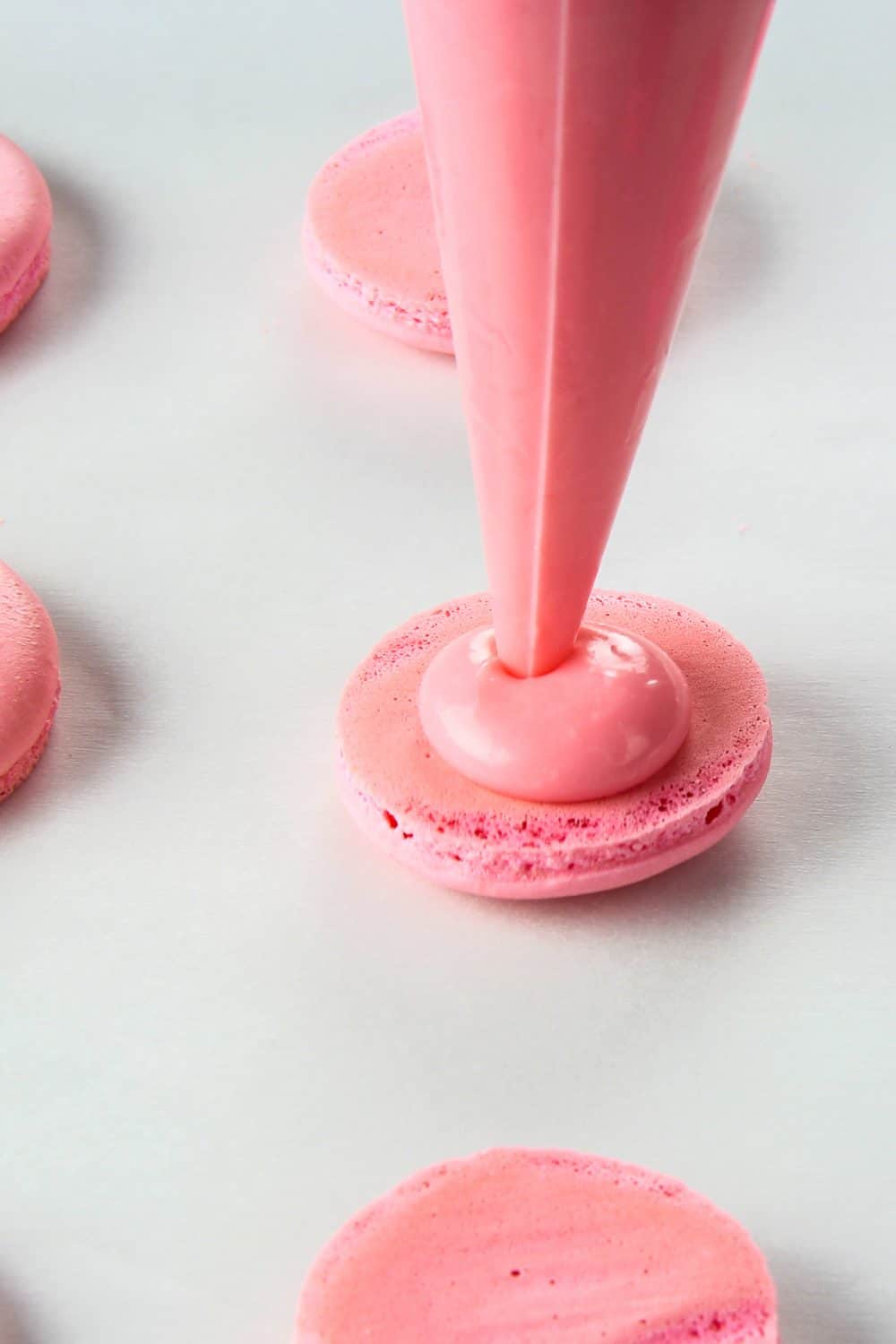 piping out pink ganache filling onto a pink macaron shell