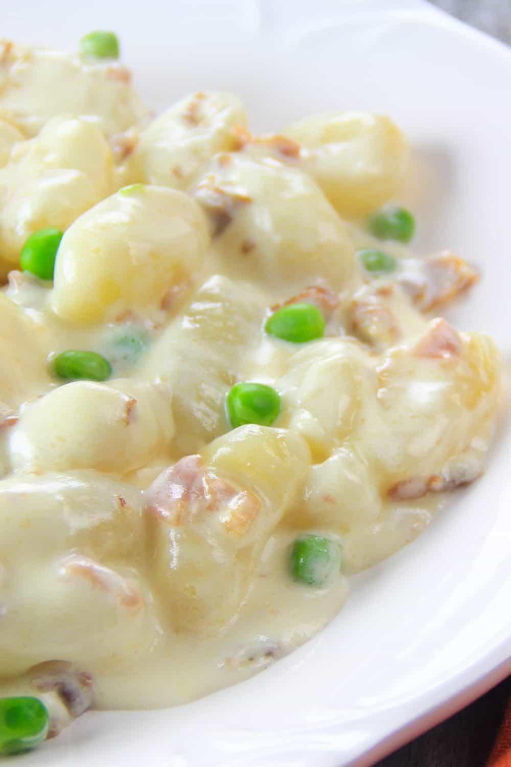 White bowl filled with potato gnocchi recipe including peas, prosciutto and cream sauce.