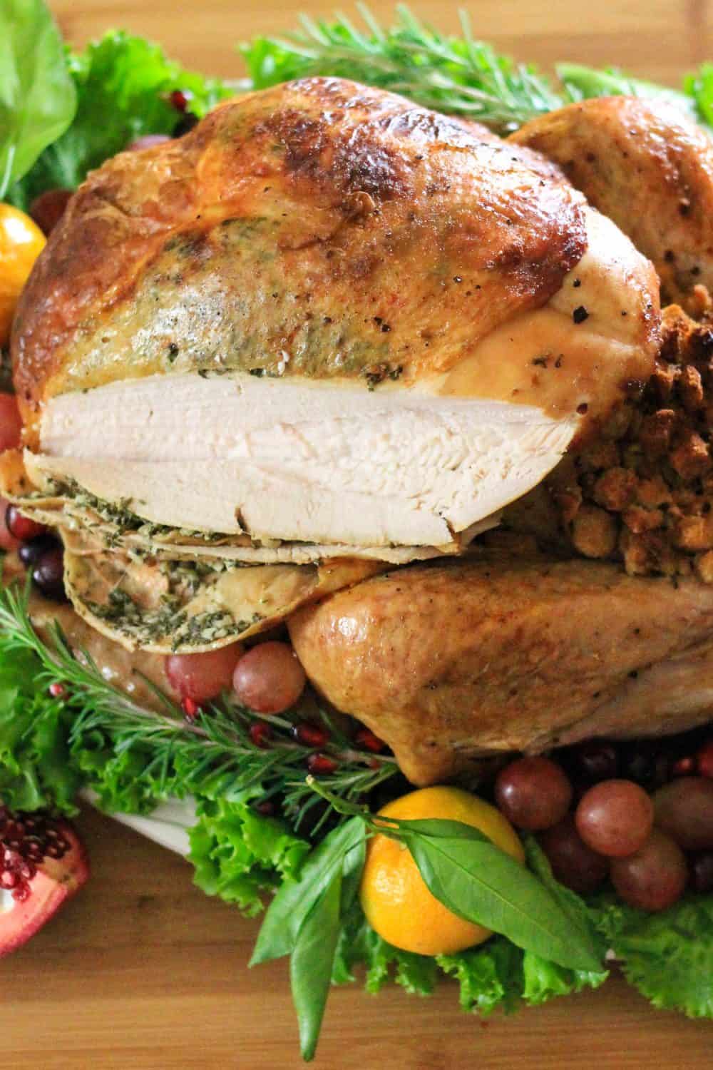 a close up image of a roasted thanksgiving turkey sliced open with rosemary and grapes beside it