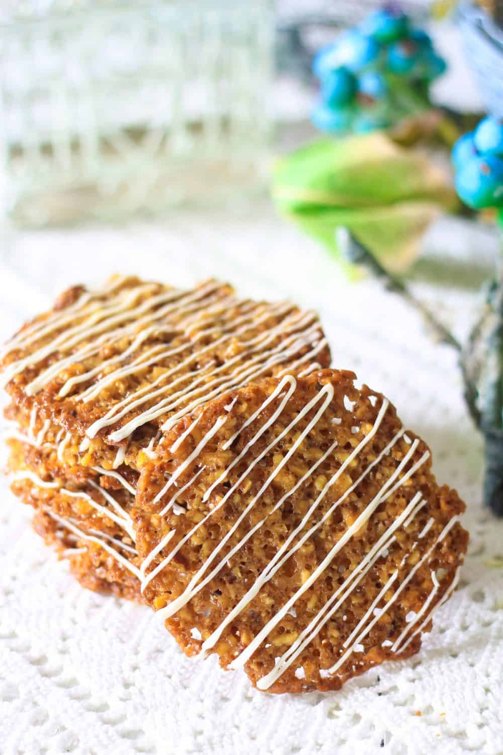 Florentine Cookies are the perfect delicate balance of crunchy sweetness that melts in your mouth. This simple recipe will become a favorite. #Florentinecookies #lacecookies #almondcookies #thincooking #Florentines Photograph of a stack of florentine cookies with white chocolate drizzle laying on a lace tablecloth