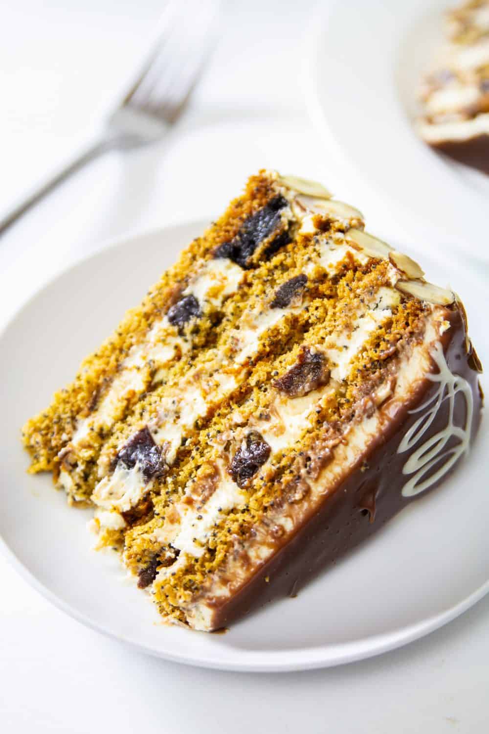 Close up of slice of Poppy Seed Honey Cake on a white plate with a fork and another slice on a white background