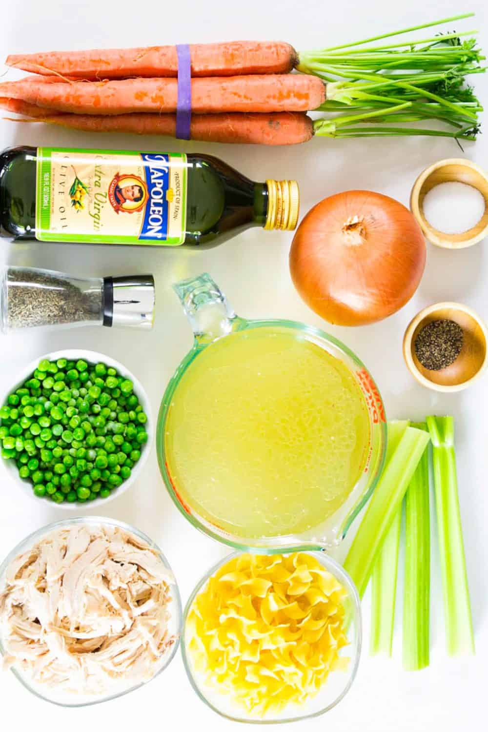 Everyone needs a Chicken Noodle Soup from Scratch in their recipe book and this one loaded with carrots, celery and the extra snap of peas is going to become a family favorite. #chickennoodlesoup #noodlesoup #chickensoup #healthysoup #clearsoup #lowcaloriesoup Ingredients for chicken noodle soup from scratch laying on a flat white surface and photographed from overhead