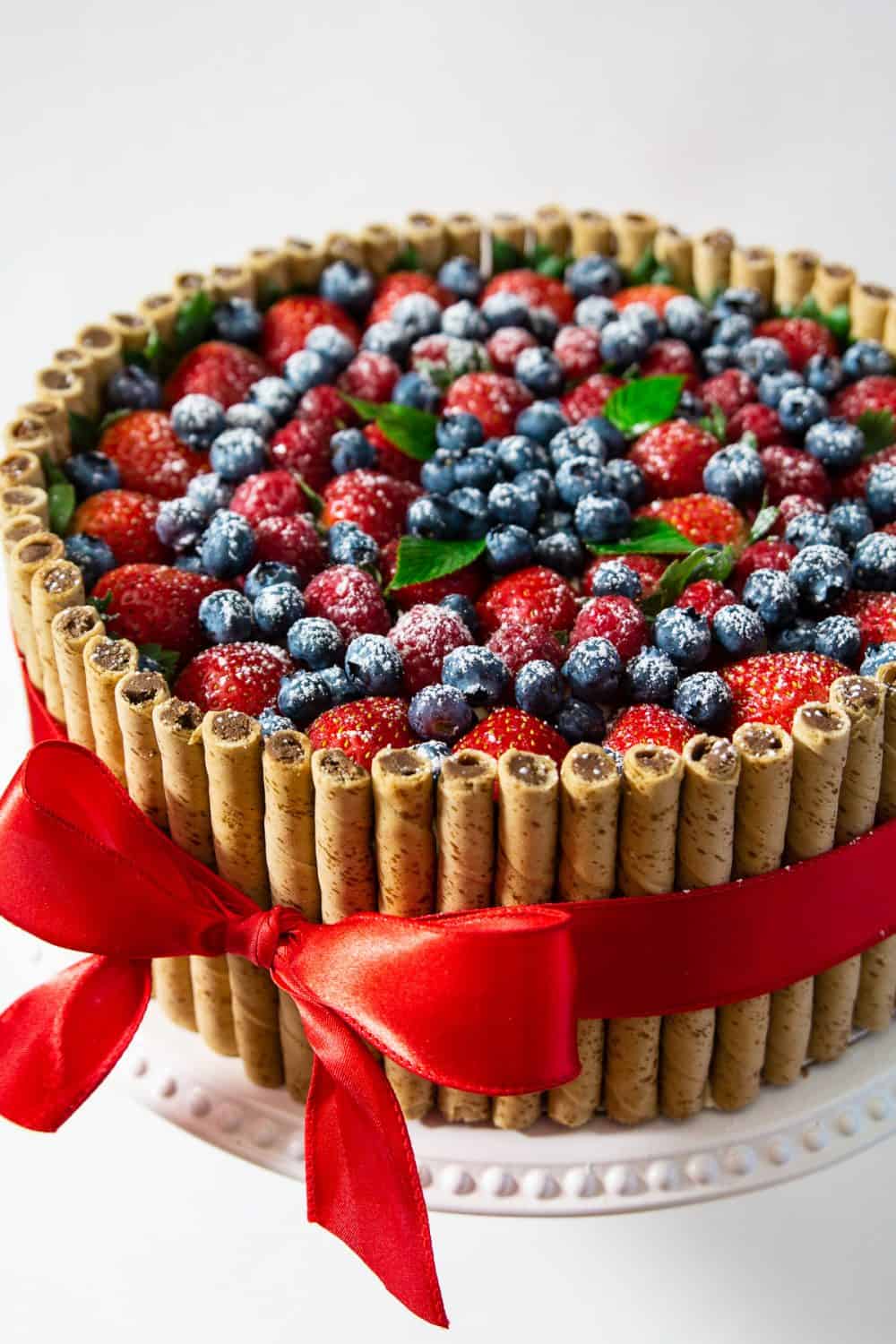 Decadent layers of hazelnuts, poppyseed, and cherry cake with creamy dulce de leche frosting. This Russian Royal cake recipe is the ultimate holiday cake! #royalcake #russiancake #korolevskytort #korolevsky #russianlayercake A completely assembled and decorated Russian Royal cake topped with fruit and tied with a red ribbon