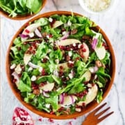 spinach pomegranate salad in a wooden bowl. Some pomegranates and a wooden spoon around the bowl.