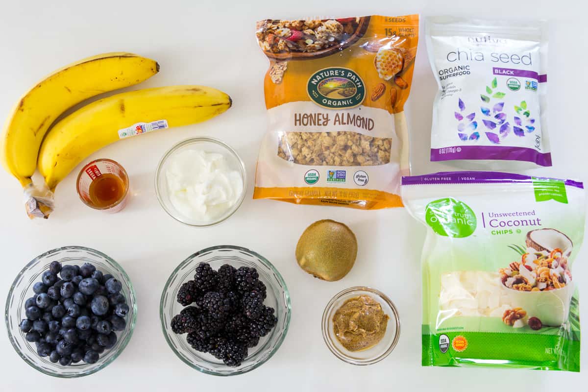 Ingredients for Blueberry Smoothie Bowl: bananas, honey, Greek yogurt, granola, chia seeds, coconut flakes, almond butter, kiwi, blackberries, and blueberries.