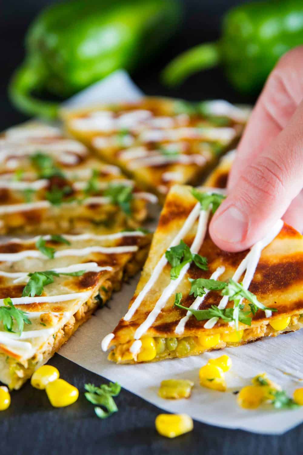 These easy chicken quesadillas are loaded with Mexican cheese, hatch chilies, and juicy rotisserie chicken. Its the perfect recipe for busy weeknights! #chickenquesadillas quesadilla #mexicanrecipe #mexicanfood #30minutemeal sliced chicken quesadilla with a corn, sour cream, and chopped cilantro on top