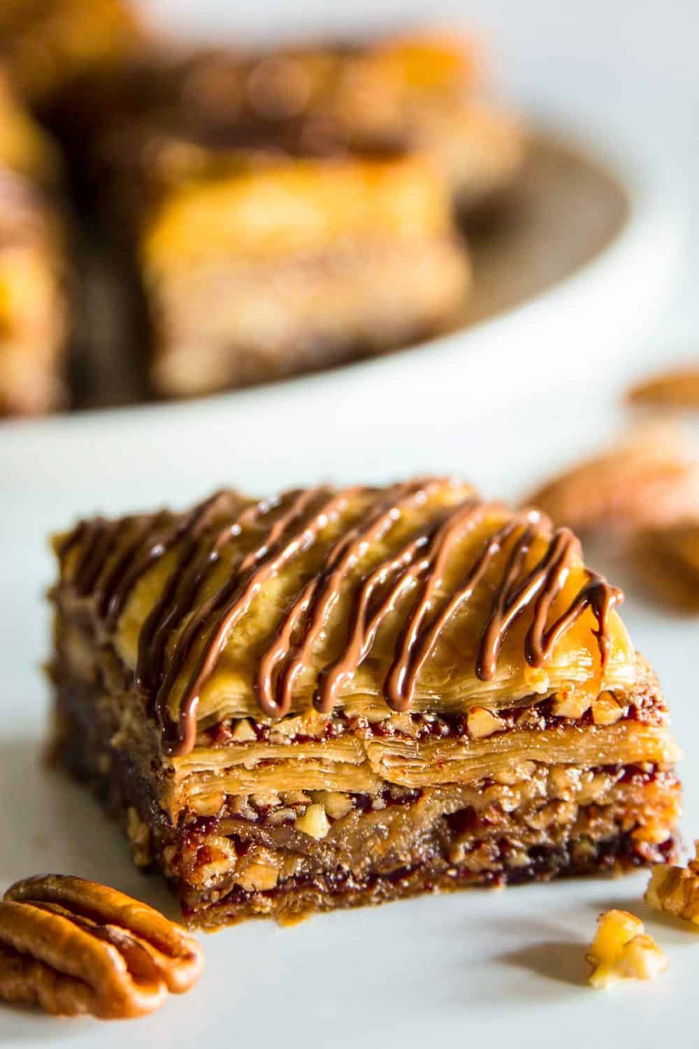 Up close picture of baklava recipe with nutella on a flat white surface with focus on single piece of baklava and a blurry image of a tray with more pieces in the background