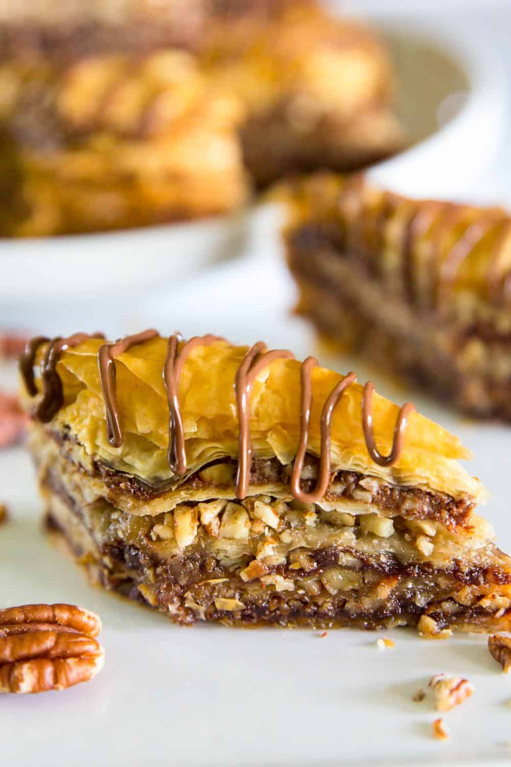 Up close image of a triangular slice of baklava recipe with Nutella filling sitting on a white table with drizzles of Nutella across the top