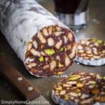 a roll of Chocolate Salami with 2 slices cut on the side. part of a knife seen next to the chocolate salami