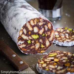 a roll of Chocolate Salami with 2 slices cut on the side. part of a knife seen next to the chocolate salami