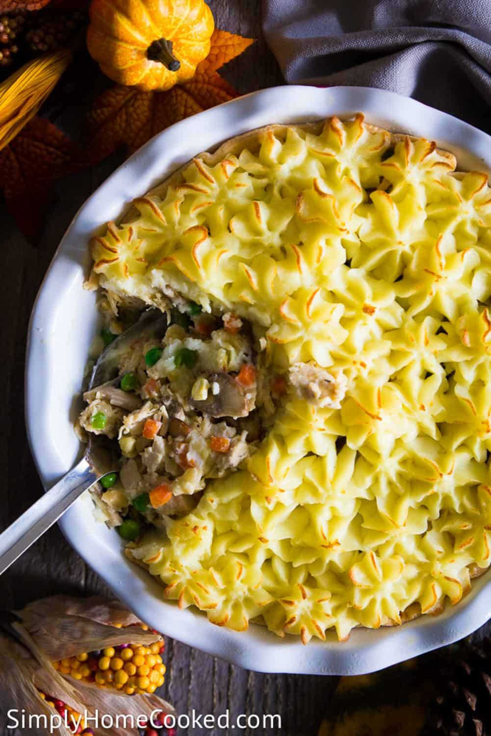 The BEST way to use up thanksgiving turkey leftovers if by making this incredibly delicious shepherds pie! It's quick, simple, and so yummy. #turkeyleftovers #leftoverturkeyrecipe #shepherdspie #Turkeypie #savorypie An overhead image of a leftoveer turkey shephers pie with a large spoon in the center and a small pumpkin above it