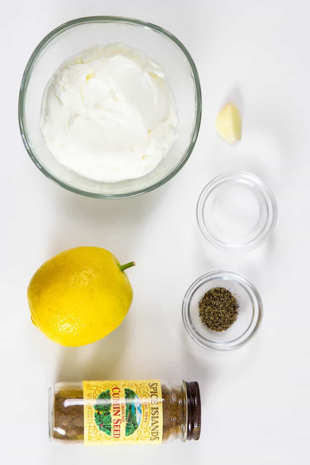 An overhead view of the ingredients for Greek yogurt sauce - Greek yogurt, garlic, salt, pepper, lemon and cumin