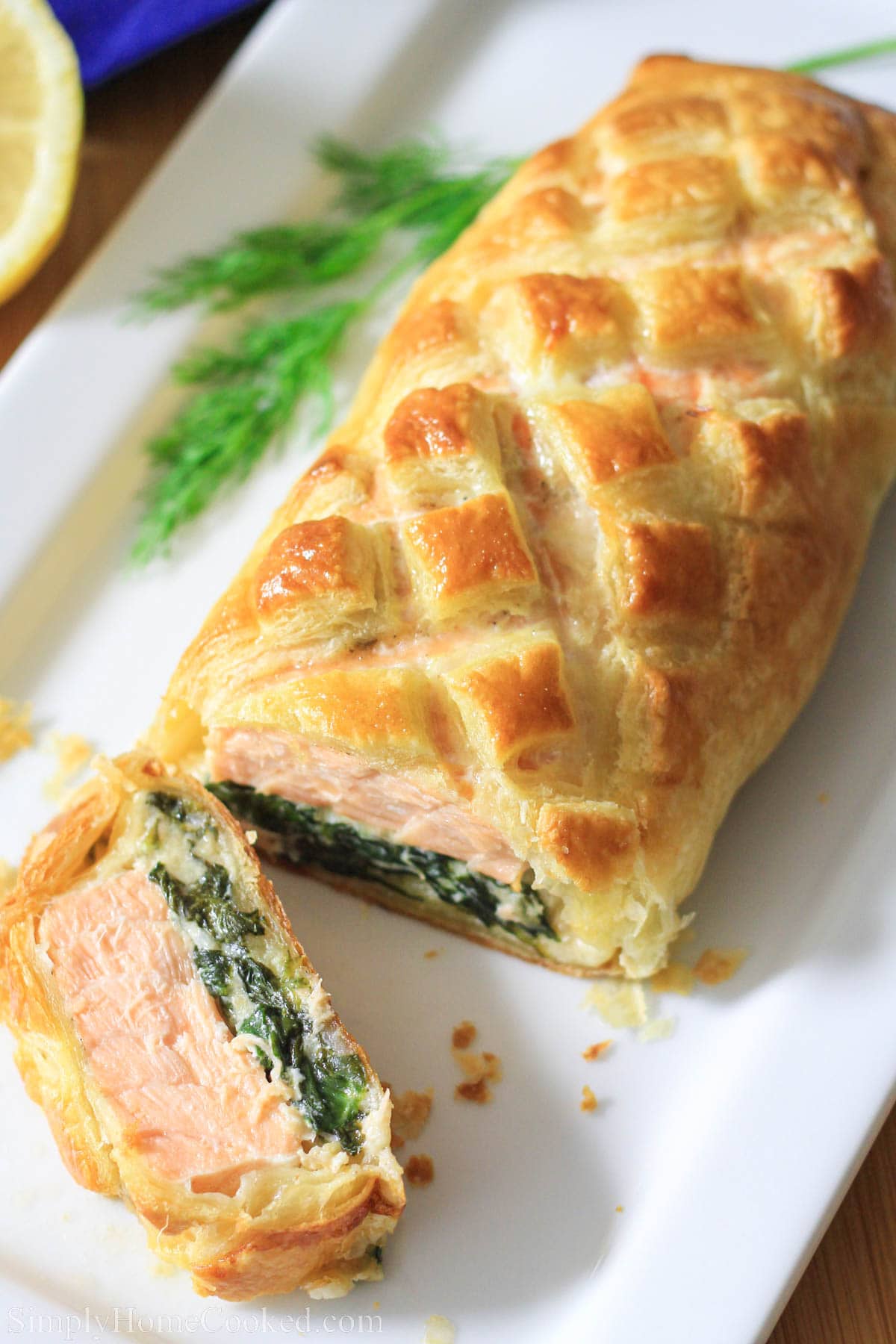 Seasoned salmon placed on a bed of cheesy sauteed spinach, wrapped in puff pastry, and baked to perfection. #salmonwellington #bakedsalmon #savorypuffpastry #salmondinner #fancydinner Salmon Wellington cut on a white plate.