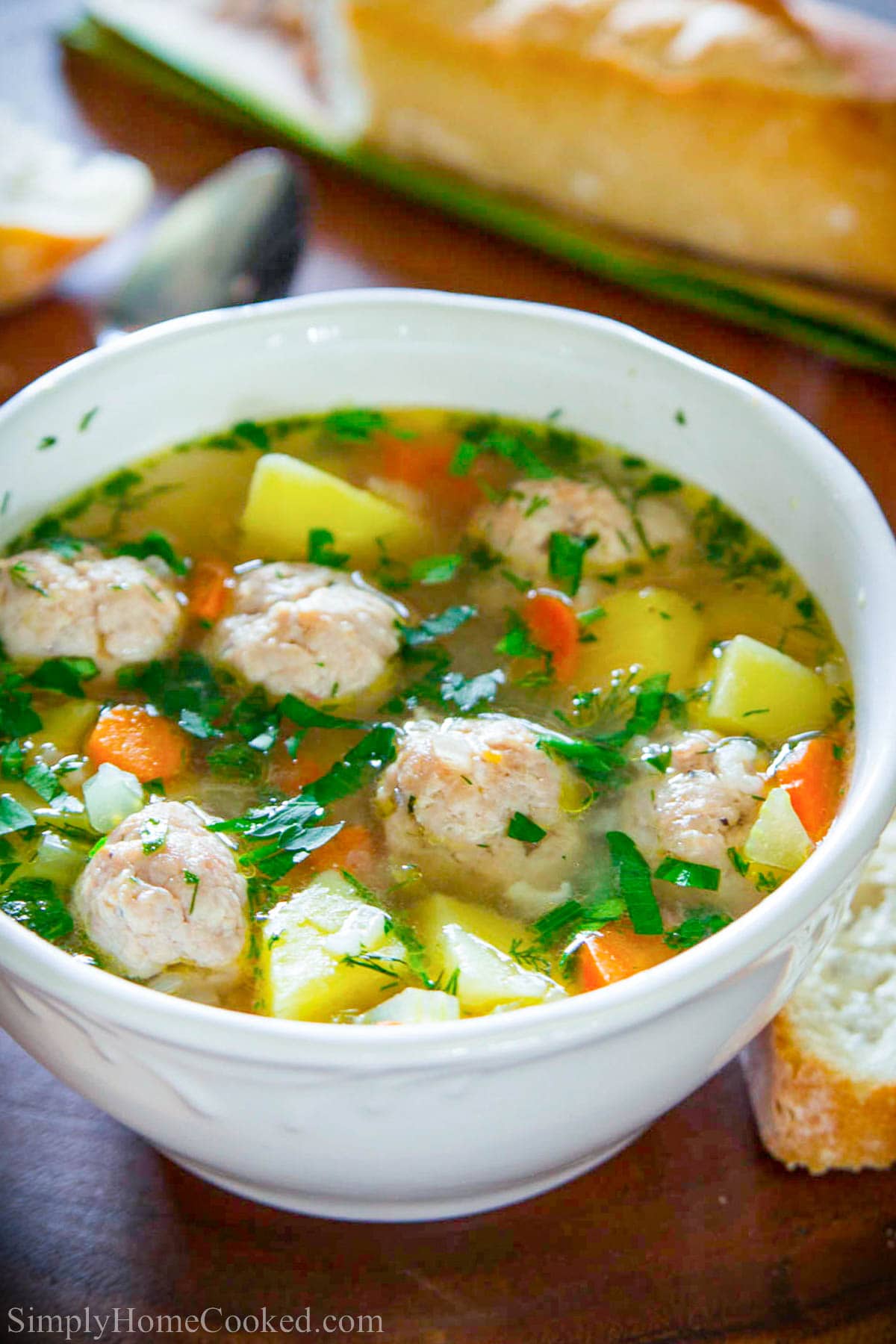Bowl of Chicken Meatball Soup and crusty bread next to it. 