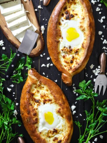 2 easy khachapuri breads with eggs in the center and sliced feta cheese and parsley beside it