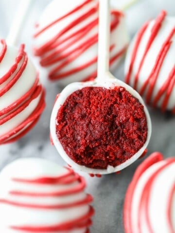 red velvet cake pops dipped in white candy melts and drizzled with red candy melts, then bitten into