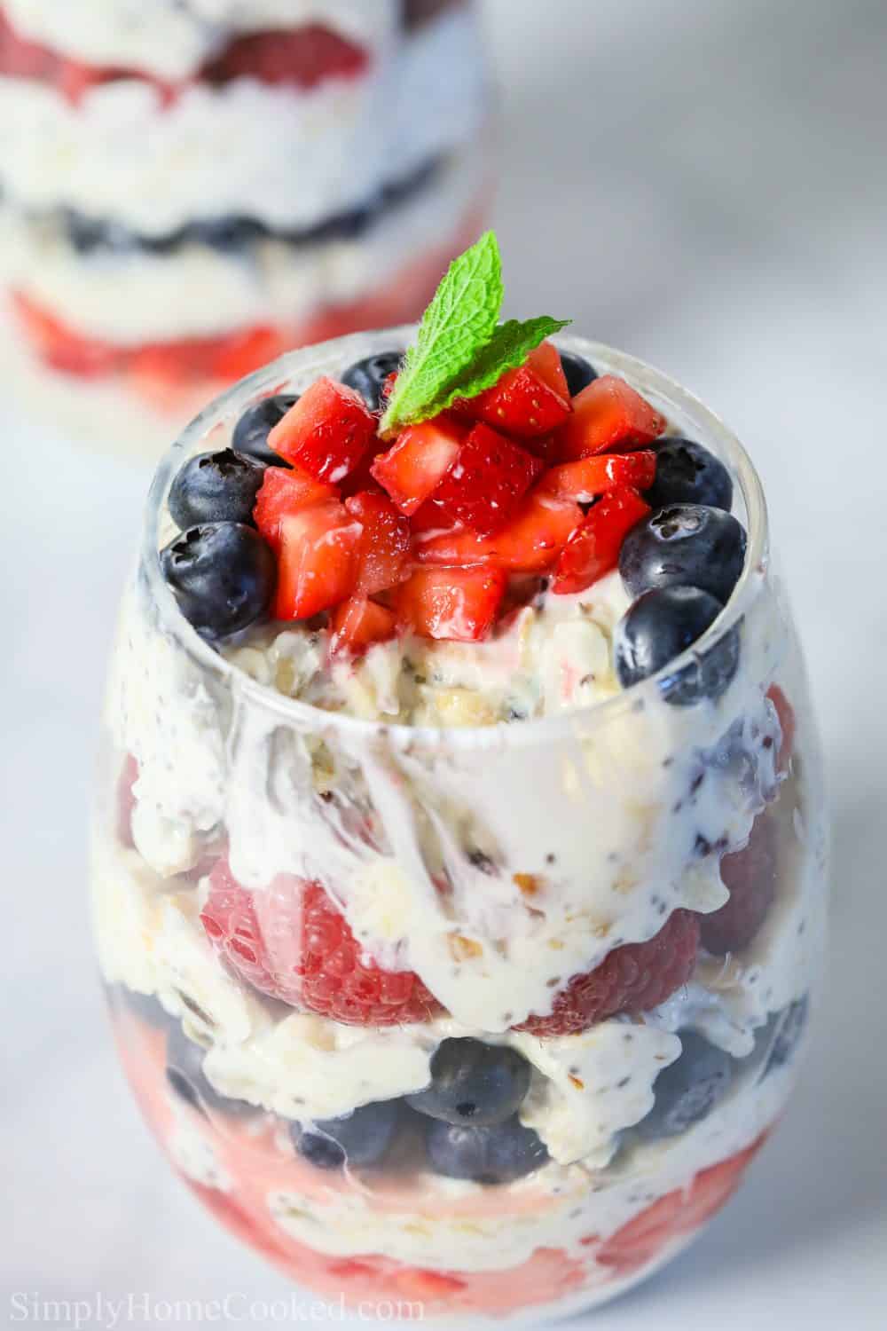 close up photo of yogurt berry parfait in a glass cup with chopped strawberries and a mint leaf on top