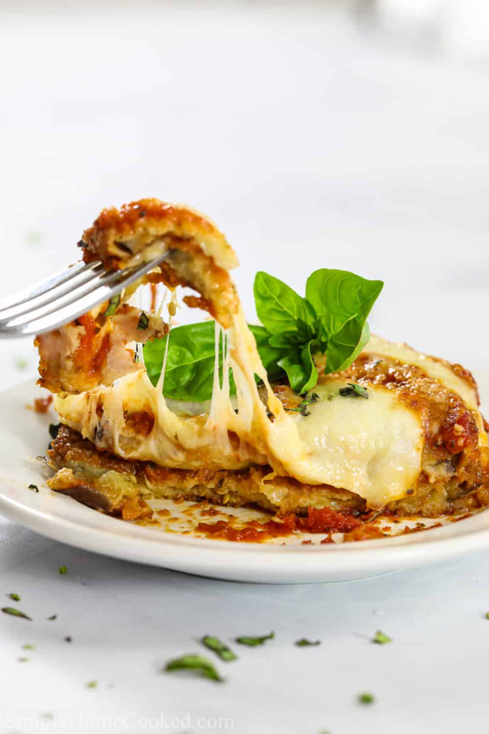 A classic Baked Eggplant Parmesan with breaded eggplants, marinara sauce, and hot bubbling mozzarella and parmesan. It's the ultimate Italian comfort food. #eggplantparmesan #bakedeggplant #eggplantrecipe #italianfood a piece of baked eggplant parmesan on a plate and a fork removing a bit with a cheese pull