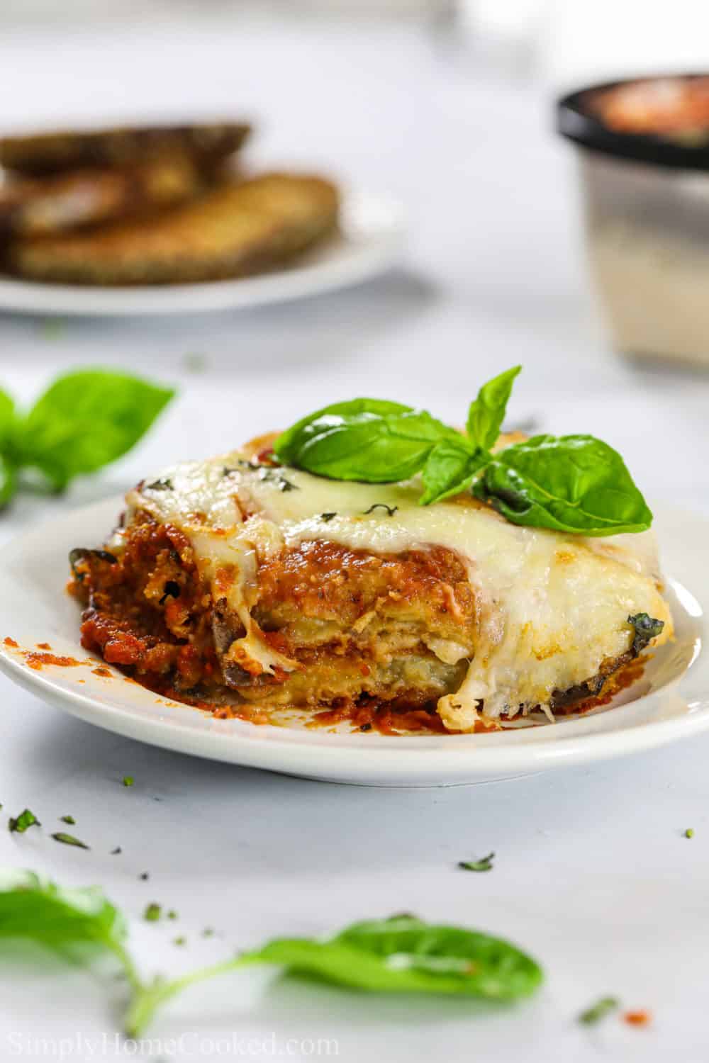 A classic Baked Eggplant Parmesan with breaded eggplants, marinara sauce, and hot bubbling mozzarella and parmesan. It's the ultimate Italian comfort food. #eggplantparmesan #bakedeggplant #eggplantrecipe #italianfood a piece of eggplant parmesan on a plate with some basil on top of the baked parmesan