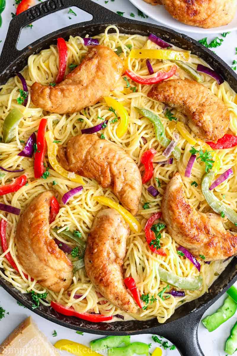 This Chicken Scampi Recipe is bursting with flavor from the creamy wine sauce, sauteed peppers, and juicy chicken tenders. It's also super easy and quick to make! #chickenscampi #chickenpasta #olivegardenpasta #scampipasta #italianpasta overhead image of chicken scampi pasta in a cast iron pan