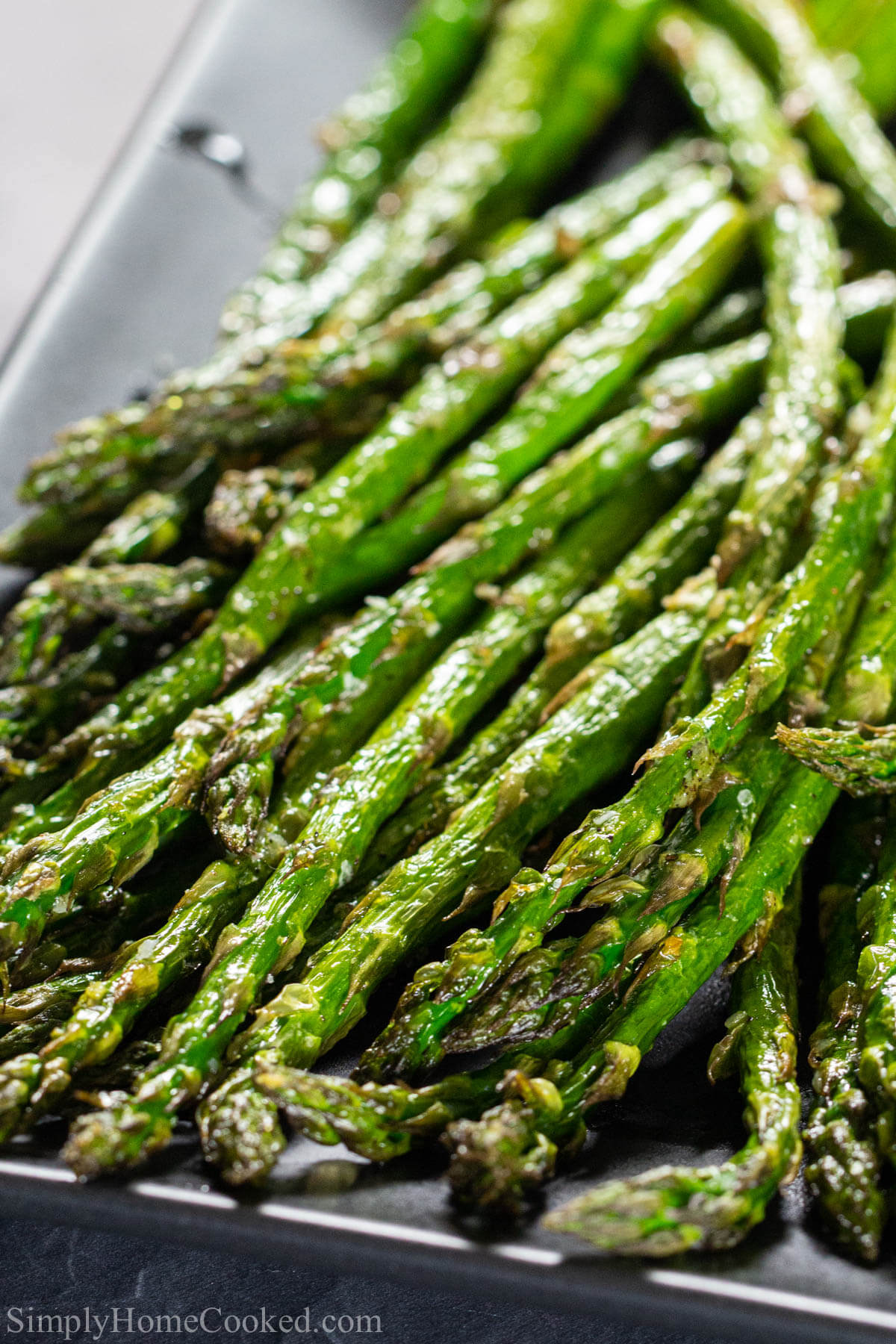 Close up vertical image of Air Fryer Asparagus lined up diagonally on a pan