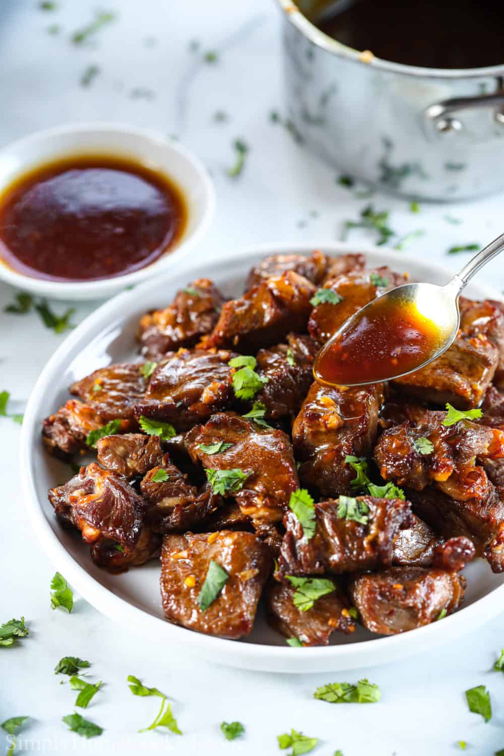 Plate of Air Fryer Steak Bites being drizzled with sauce, with a bowl of sauce in the background.