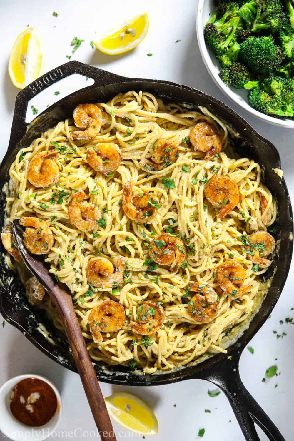 Skillet full of Cajun Shrimp Pasta and some lemon slices, broccoli, and cajun seasoning on the side.