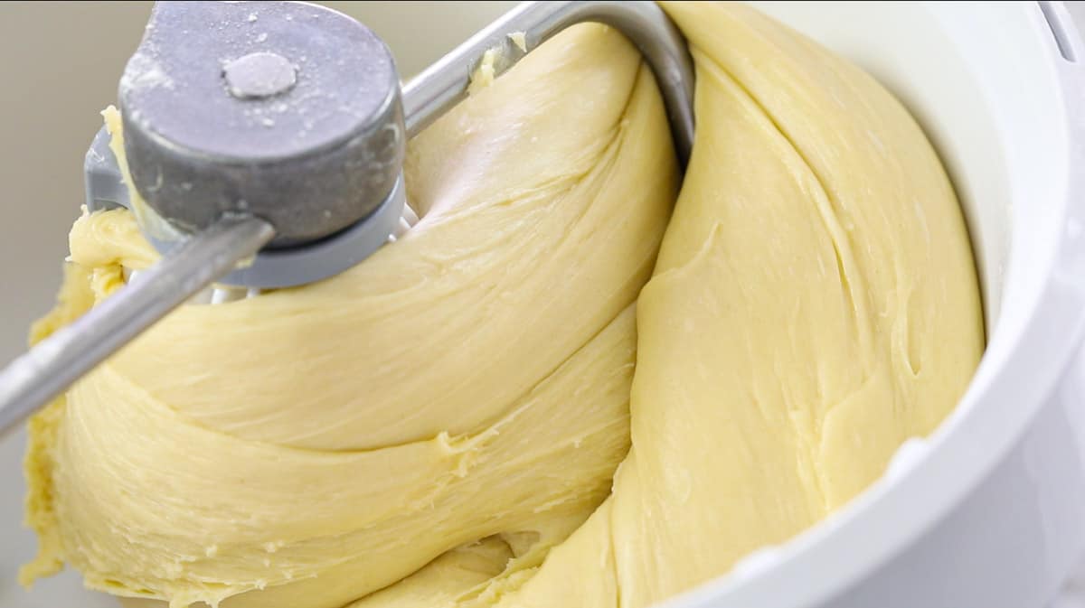 Buttery Brioche Bread dough mixing in a stand mixer with a hook attachment. 