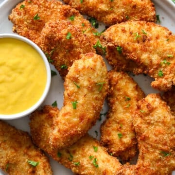 Plate of breaded air fryer chicken breasts with sauce on the side and a parsley garnish.