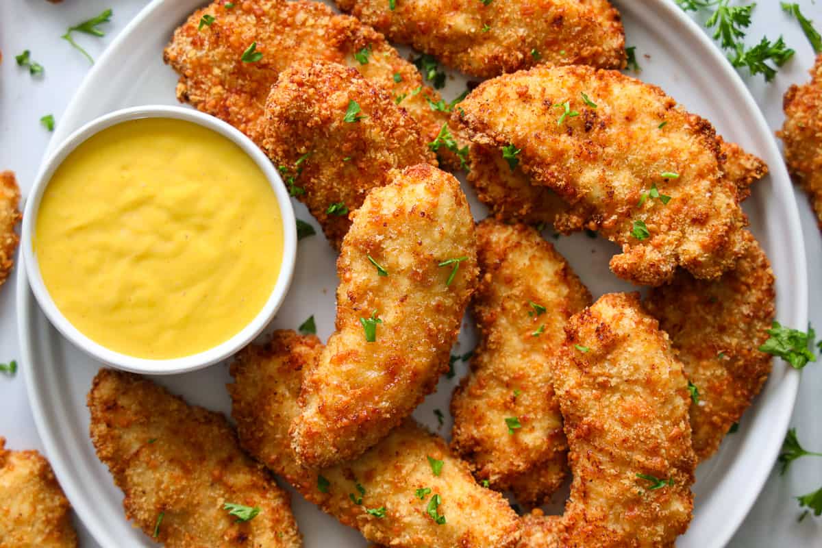Plate of breaded air fryer chicken breasts with sauce on the side and a parsley garnish.