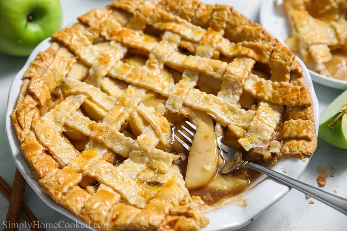 This Homemade Apple Pie is deliciously sweet with a cinnamon twist. With a latticed crust that makes it look as pretty as it is tasty, you'll be proud to serve this amazing dessert anytime. #homemadeapplepierecipe #pierecipe #bestapplepie #besthomemadeapplepie Homemade apple pie with a slice missing and a fork in it.