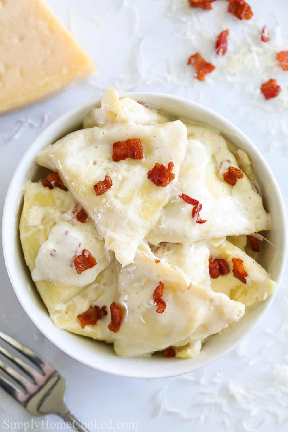 Close up of Chicken and Cheese Ravioli with a cream sauce and bacon bits on top, with more bacon and cheese nearby.