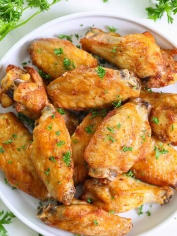 overhead image of crispy air fryer chicken wings on a white plate with chopped parsley on top