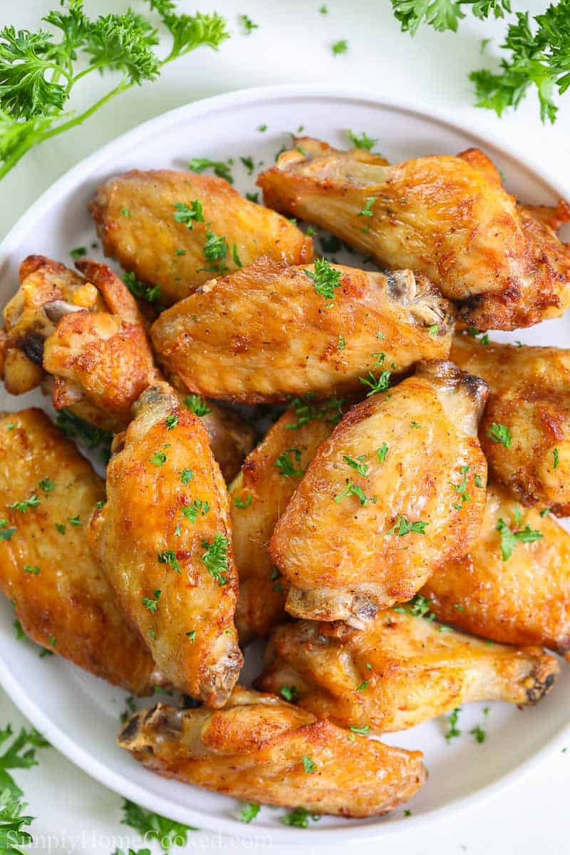 These Crispy Air Fryer Chicken Wings are so easy to make and taste juicy and delicious. Cooked to perfection, their texture and flavor are much better than deep-fried wings. #crispyairfryerchickenwings #airfryerrecipes #airfryerchicken #chickenwingsrecipe overhead image of crispy air fryer chicken wings on a white plate with chopped parsley on top