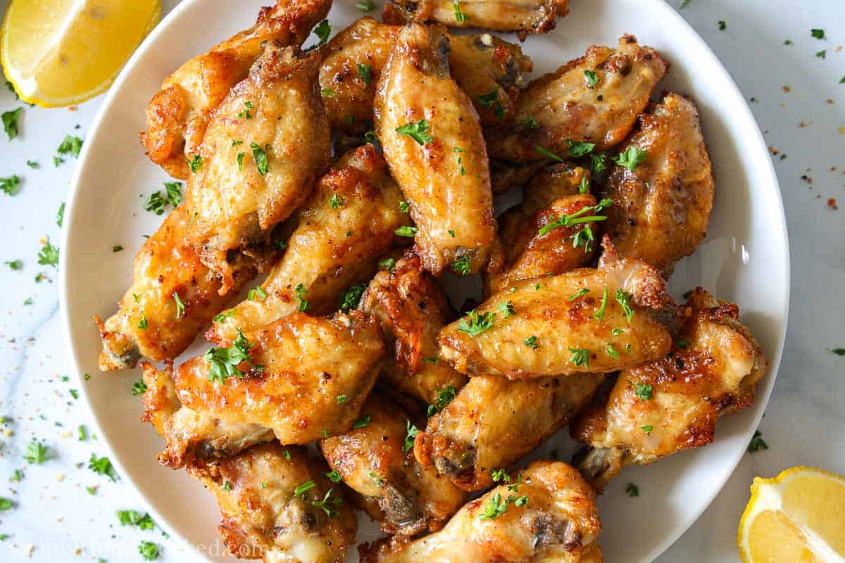 overhead image of crispy air fryer lemon pepper wings on a white plate with lemon wedges around