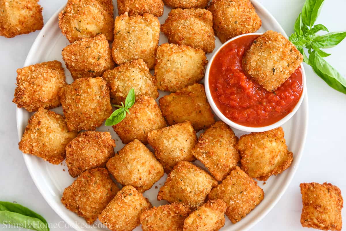 Overhead view of a plate of Crispy Fried Ravioli with one in marinara and some herbs on the side.
