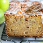close up image of an apple fritter bread sliced, with white glaze on top and granny smith apples in the background