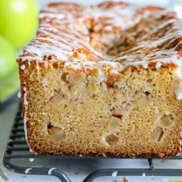 close up image of an apple fritter bread sliced, with white glaze on top and granny smith apples in the background