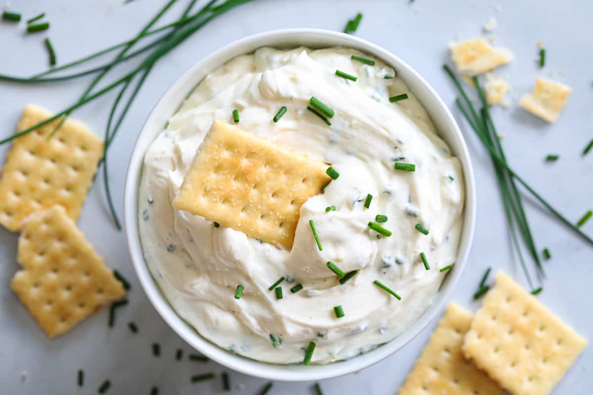 Aerial view of Garlic Cream Cheese Dip with crackers on the side and one in the dip, with chives on top.