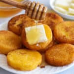 Southern Hot Water Cornbread on a plate with butter and honey being drizzled on it, and more honey and butter in the background.