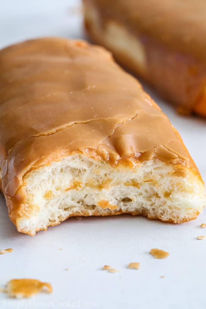 Close up of Maple Donut Bars from Scratch with a bite missing and some crumbs and donuts in the background.