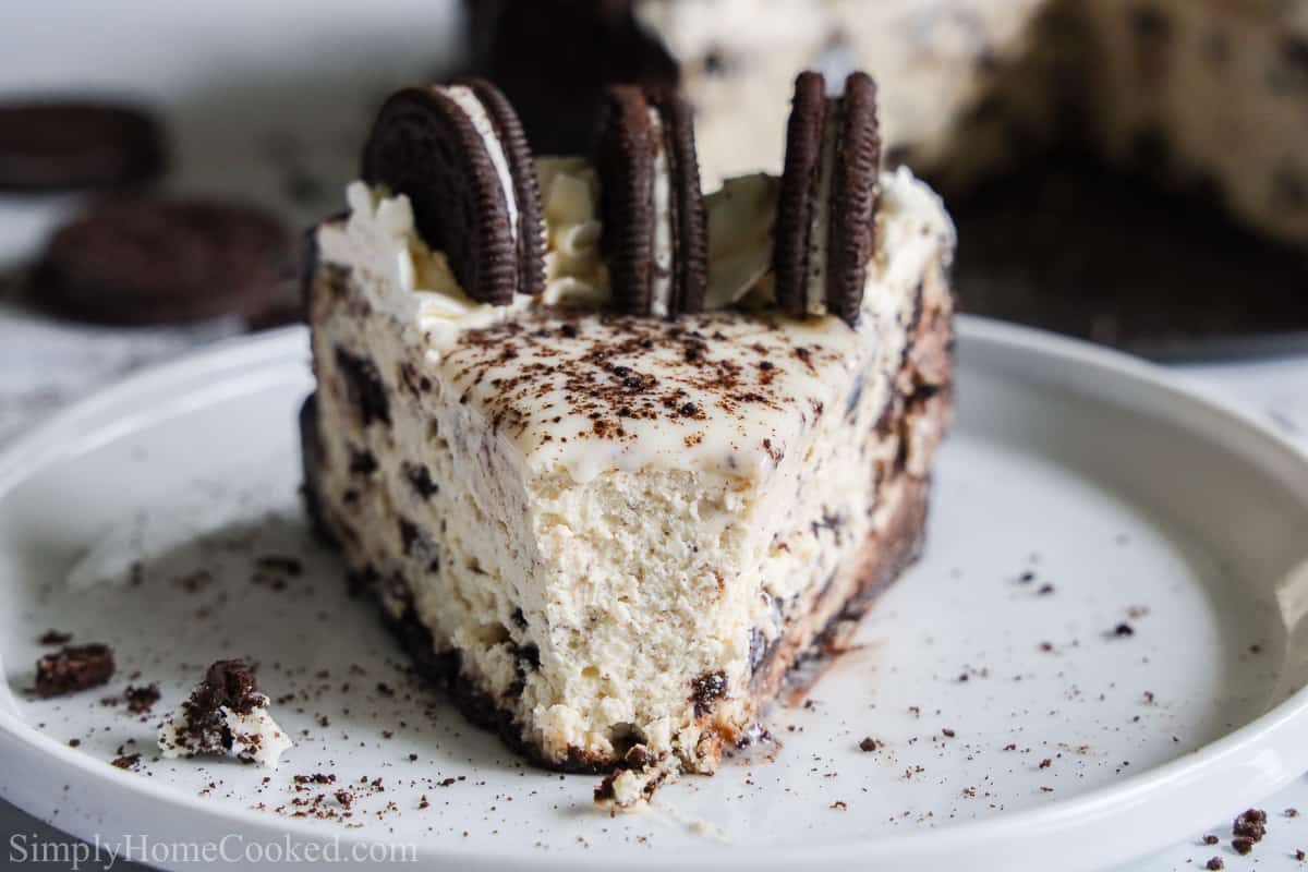 Front view of a slice of Easy Oreo Cheesecake with 3 Oreos on top and crumbs on the white plate.