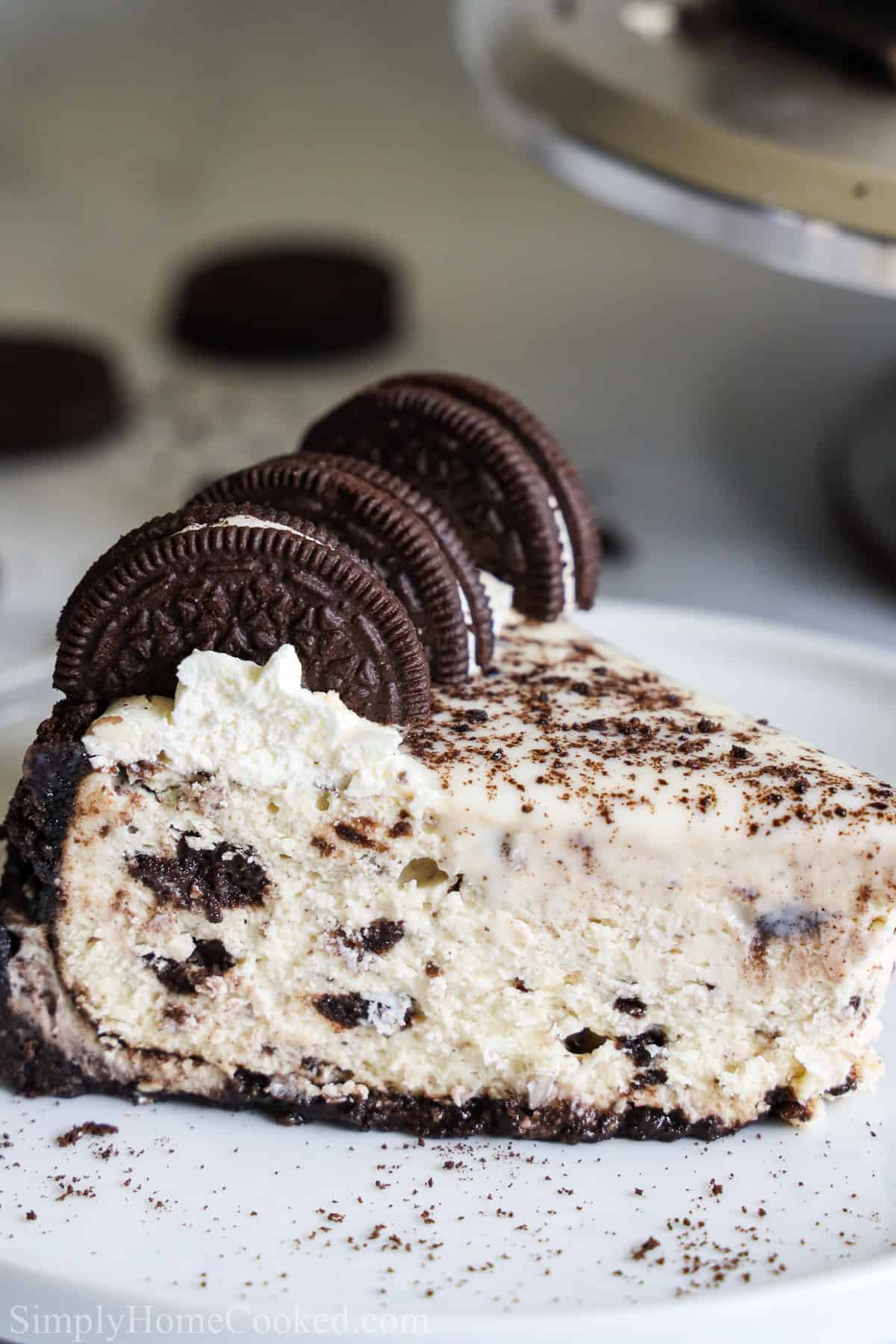This Easy Oreo Cheesecake is everything you want and love in a dessert - rich, chocolaty, creamy, and decadent. It's sinfully delicious! #oreocheesecake #cheesecake #cheesecakeoreo #easyoreocheesecake Close up side view of a slice of Easy Oreo Cheesecake with Oreos on top, on a white plate.