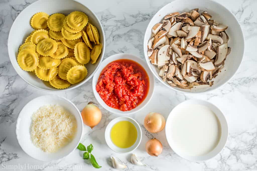 Ingredients for Italian Sausage Ravioli, including Italian sausage ravioli, baby bella mushrooms, pureed tomatoes, Parmesan cheese, heavy cream, onion, garlic cloves, olive oil, and basil leaves, on a white background.